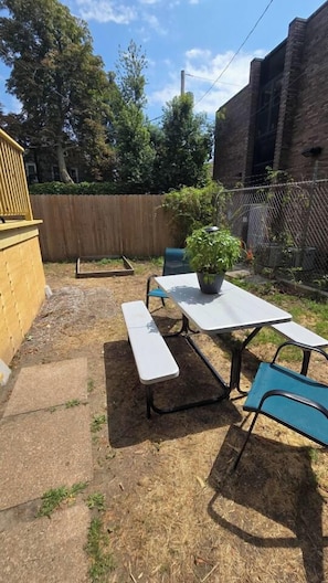 Ein Garten mit einem Picknicktisch und Stühlen, einem Blumentopf und einem Holzzaun.