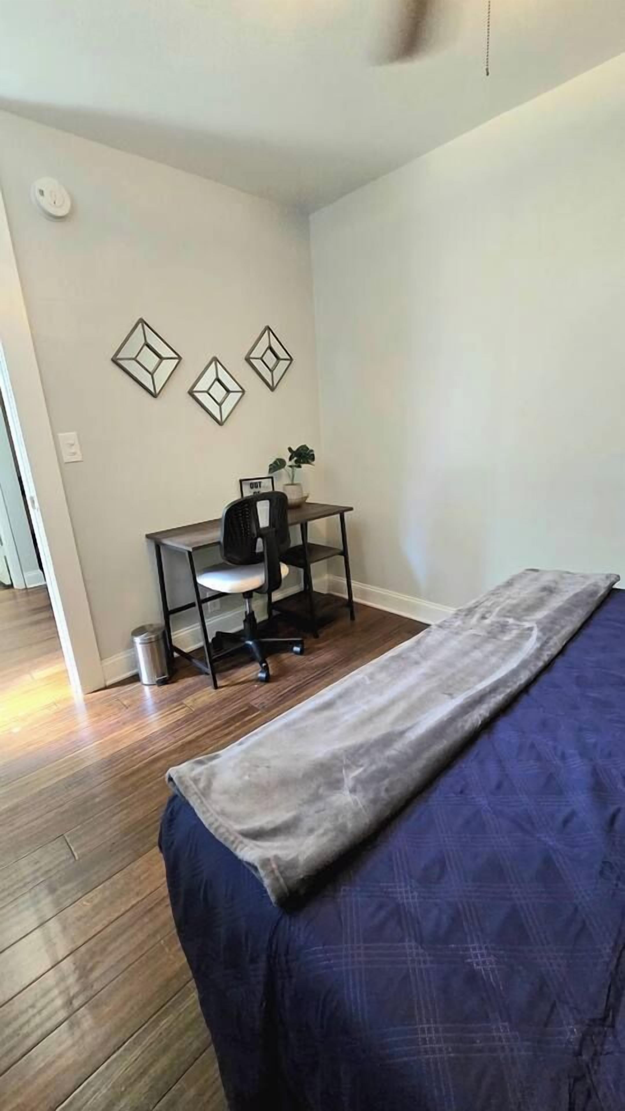 A bedroom with a bed, a desk with a chair, and a small trash bin.