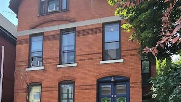 Un edificio de ladrillo de dos pisos con una puerta principal azul oscuro, con el número 50, y un pequeño jardín delantero con césped y algunas plantas.