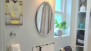A bathroom with a white sink, dark cabinets, a round mirror, and a towel rack. - Patio Perfection in Allentown (Buffalo)