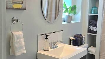 A bathroom with a white sink, dark cabinets, a round mirror, and a towel rack.