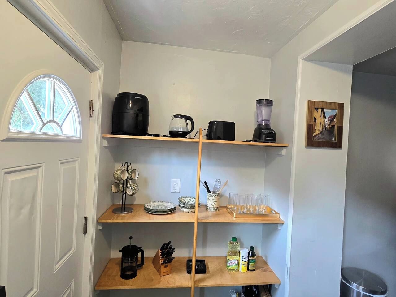 A kitchen with a coffee maker, kettle, blender, and shelves with dishes and utensils.