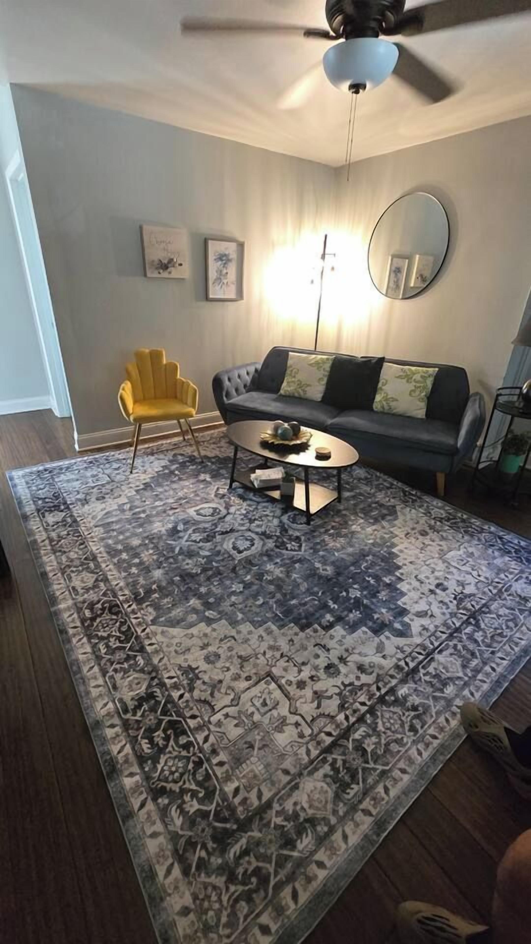 A living room with a sofa, armchair, coffee table, and a patterned rug.