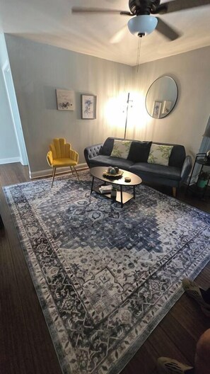 A living room with a sofa, armchair, coffee table, and a patterned rug.