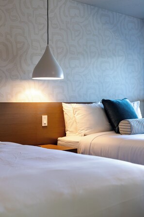 Een hotelkamer met een bed, nachtkastje, lamp en behang met een patroon.