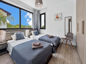 A hotel room with two beds, a chair, a desk, and a large window offering a view of greenery. - Villa Buena Vida, Ayia Triada Pool Home (Pernera)