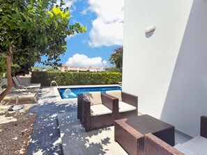 A pool area with lounge chairs, a swimming pool, and a view of a residential area in the background. - Villa Buena Vida, Ayia Triada Pool Home (Pernera)