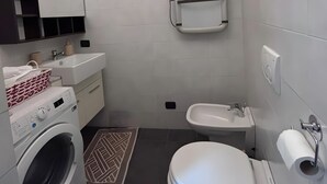 Een kleine badkamer met een wasmachine, toilet, bidet en handdoekhouder.