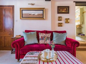 A red velvet sofa with pillows, a table with a striped tablecloth, and a vase with flowers. - The Royal Exchange House in Canterbury (Kent)