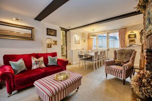 A living room with a red sofa, striped ottoman, and striped armchair, a dining area with a table and chairs, and a fireplace with a decorative mantle. - The Royal Exchange House in Canterbury (Kent)