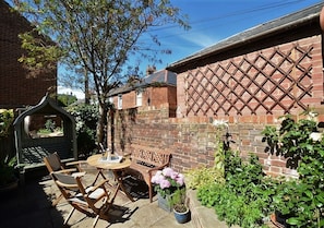 A brick house with a patio area featuring a wooden bench, a table, and potted plants. - The Royal Exchange House in Canterbury (Kent)
