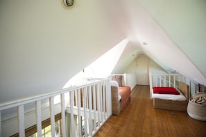 Ein Schlafzimmer im Dachgeschoss mit hohen Decken, Holzboden, weißer Brüstung und geneigter Decke.