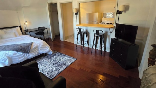 Ein Hotelzimmer mit einem Bett, einem Schreibtisch mit Stuhl, einem Fernseher und einer Küchenzeile, inklusive Kühlschrank und Herd.