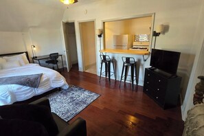 Habitación de hotel con cama, escritorio con silla, televisión y zona de cocina con refrigerador y estufa.