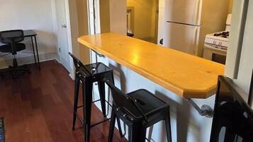 A compact kitchen with a wooden countertop, two bar stools, a refrigerator, and a gas stove.