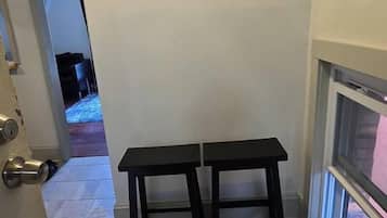 A hallway with a door on the left, a window on the right, and a pair of black stools in the center.