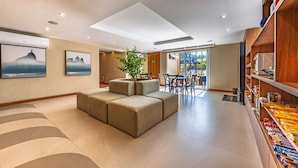 A modern living room with a sectional sofa, a dining area with a table and chairs, and a bookshelf with snacks. - Charming Studio Just a Few Steps From the Beach Q6 (Rio de Janeiro)