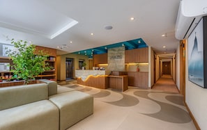 Eine moderne Hotelhalle mit einer Rezeption, einer Sitzecke und einer im Hintergrund sichtbaren Küche.
