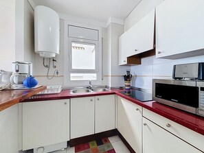 Eine kompakte Küche mit weißen Schränken, einer roten Arbeitsplatte, einer Mikrowelle und einer Kaffeemaschine.