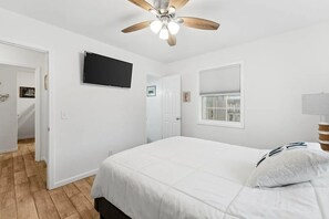 Een slaapkamer met een bed, een plafondventilator, een televisie en een raam.