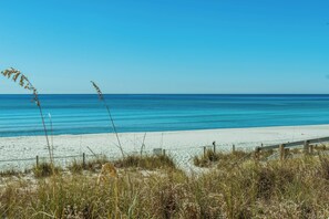 A beach with clear blue water, sandy shore, and grassy vegetation. - 🏖️ The Sandbox 🏖️🚶 Walk to Beach 🌊🏡 Fenced Yard 🌳 (Panama City Beach)