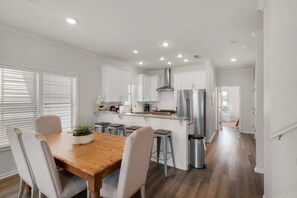 A modern kitchen with white cabinets, stainless steel appliances, and a wooden dining table. - 🌊Seabreeze 30A | Beach Across Street | Bikes | Community Pool (Inlet Beach)