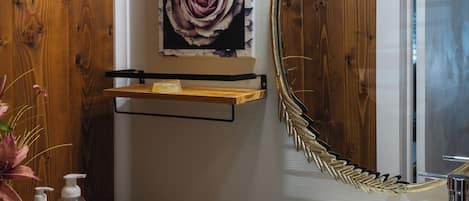 Une salle de bain avec un mur en bois, un lavabo blanc, un miroir avec un cadre doré et un luminaire placé au-dessus du miroir.
