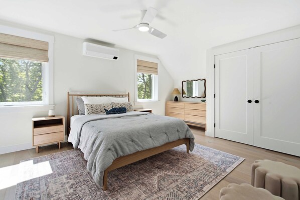 A bedroom with a bed, nightstands, a dresser, a mirror, a ceiling fan, and a door. - The Blue Jetty Coastal Home (Kennebunkport)