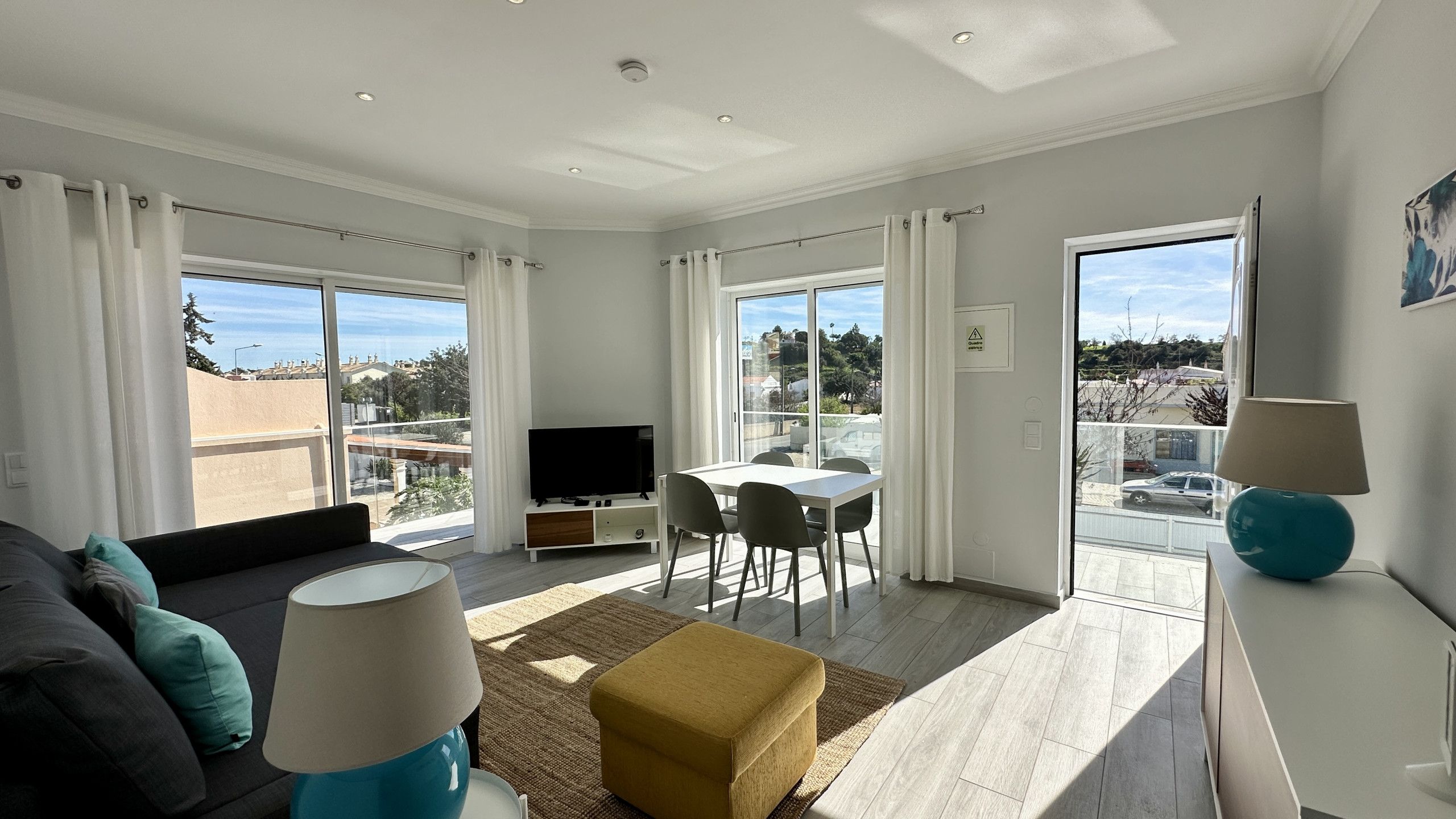 A modern living room with a sofa, ottoman, TV, dining table, and chairs.