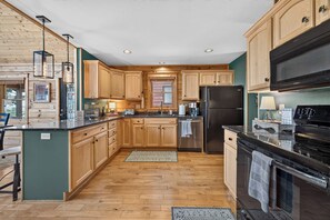 A modern kitchen with wooden cabinets, stainless steel appliances, and a herringbone wood floor. - Ski-Out to Hatley Pointe | Hot Tub | Sleeps 8 (Mars Hill)