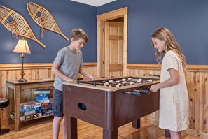 A room with a foosball table, wooden walls, and a door. - Ski-Out to Hatley Pointe | Hot Tub | Sleeps 8 (Mars Hill)