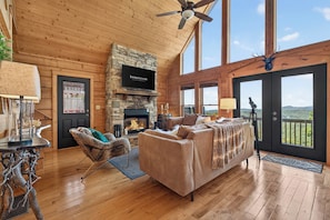 A spacious living room with a stone fireplace, a large television, and a view of the outdoors. - Ski-Out to Hatley Pointe | Hot Tub | Sleeps 8 (Mars Hill)