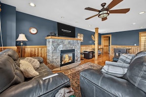 A living room with leather sofas, a stone fireplace, a ceiling fan, and a mounted television. - Ski-Out to Hatley Pointe | Hot Tub | Sleeps 8 (Mars Hill)