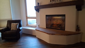A living room with a fireplace, a leather armchair, and a window.