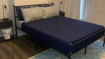 A bedroom with a bed, a nightstand, a wall-mounted picture, and a patterned rug.