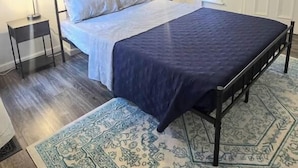 A bedroom with a bed, bedside lamps, a framed picture on the wall, a window with curtains, and a patterned rug. - Sunlit One Bedroom In Allentown (Buffalo)