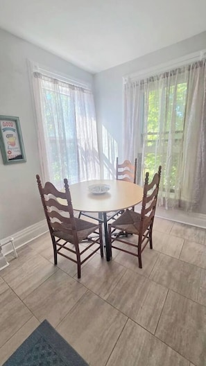 Un comedor con una mesa redonda y cuatro sillas, una alfombra en el suelo y cortinas en las ventanas.