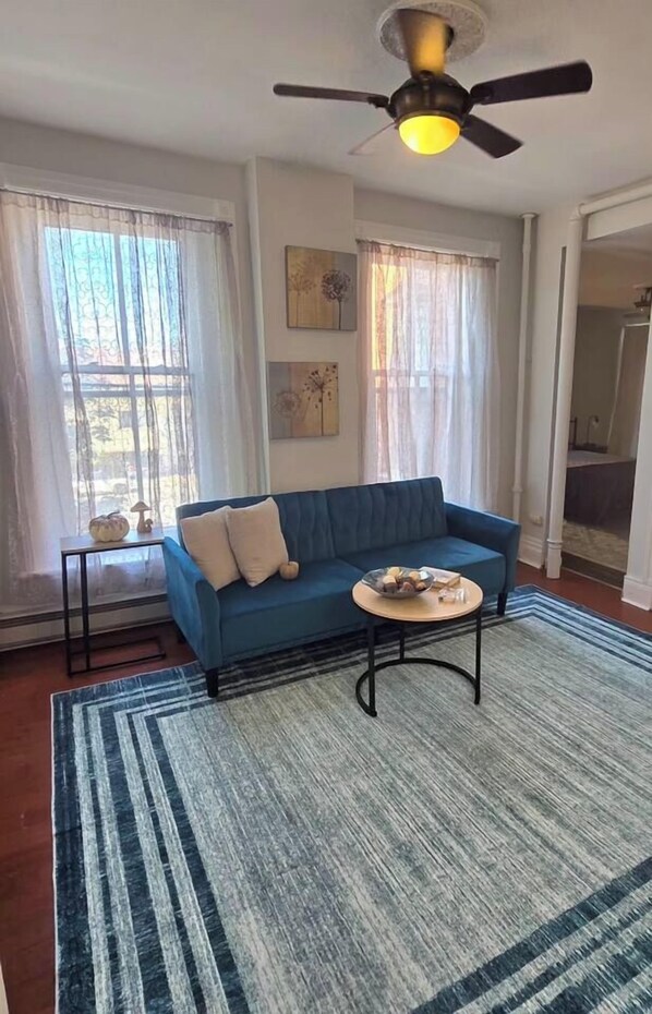 Una sala de estar con un sofá azul, una mesa de centro redonda y un ventilador de techo.