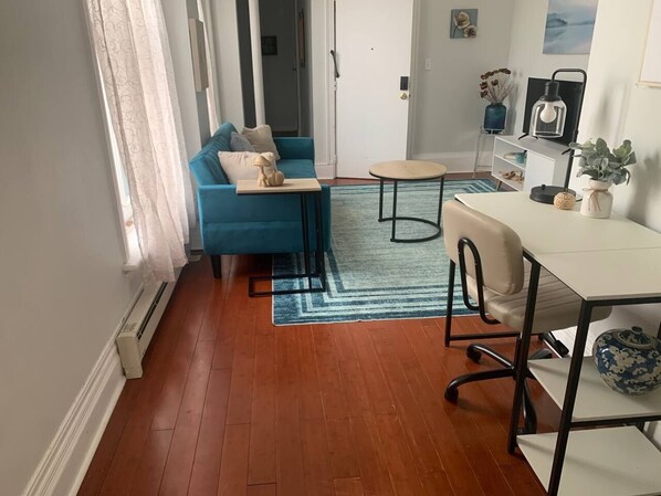 A room with a blue sofa, a small round table, a white desk, and a radiator.