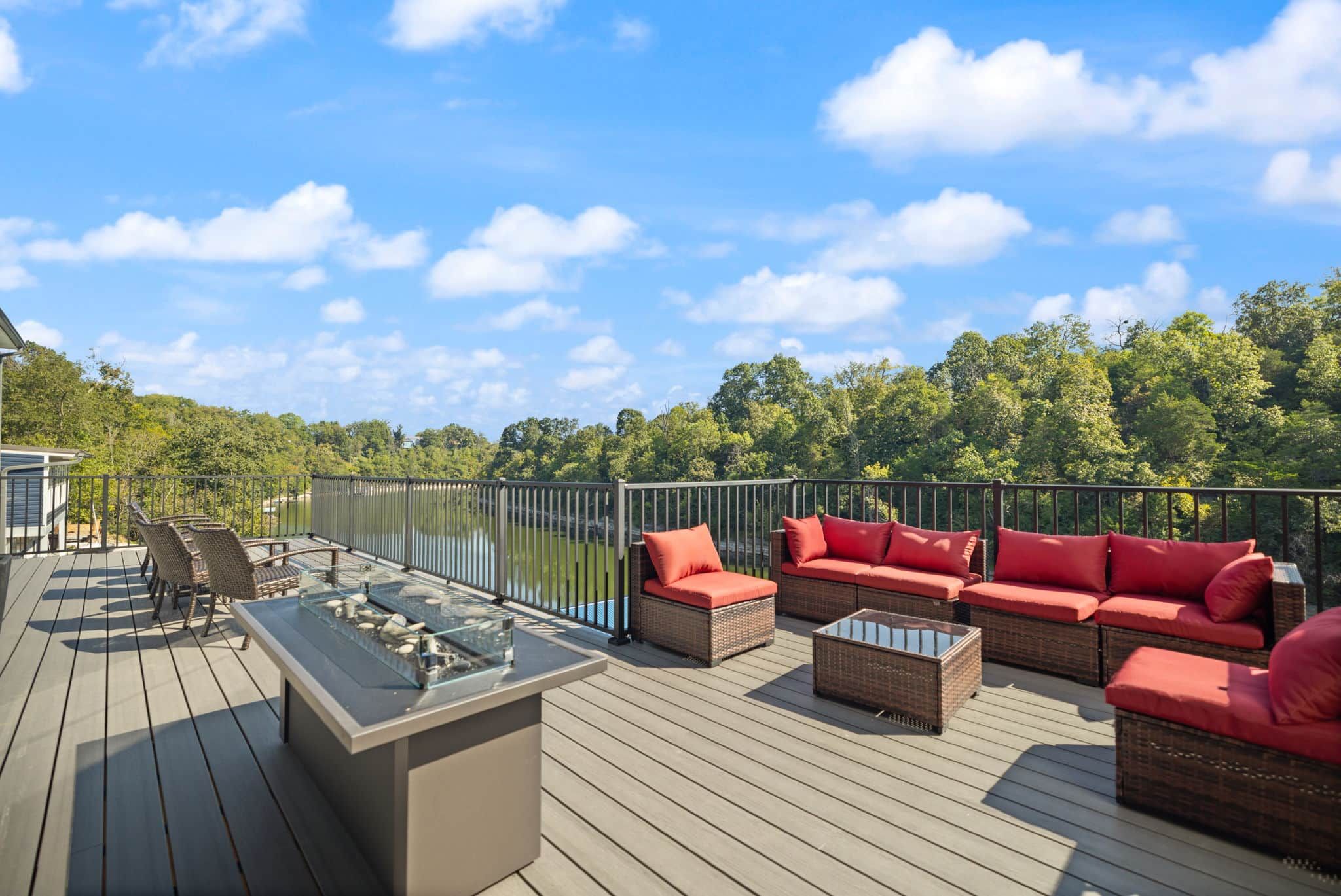 Una terraza con mobiliario exterior, una mesa de vidrio y vistas a un lago y un bosque.