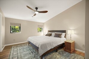 Une chambre à coucher avec un lit, des tables de chevet, un ventilateur de plafond et un tapis à motifs.