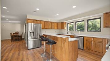 A modern kitchen with wooden cabinets, stainless steel appliances, a bar area, and large windows.