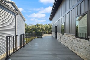 A covered outdoor deck with a metal railing, connecting two buildings with siding and stone accents. - The Gwinn | Luxury 6BR Lake Retreat, Hot Tub (Boyle County)