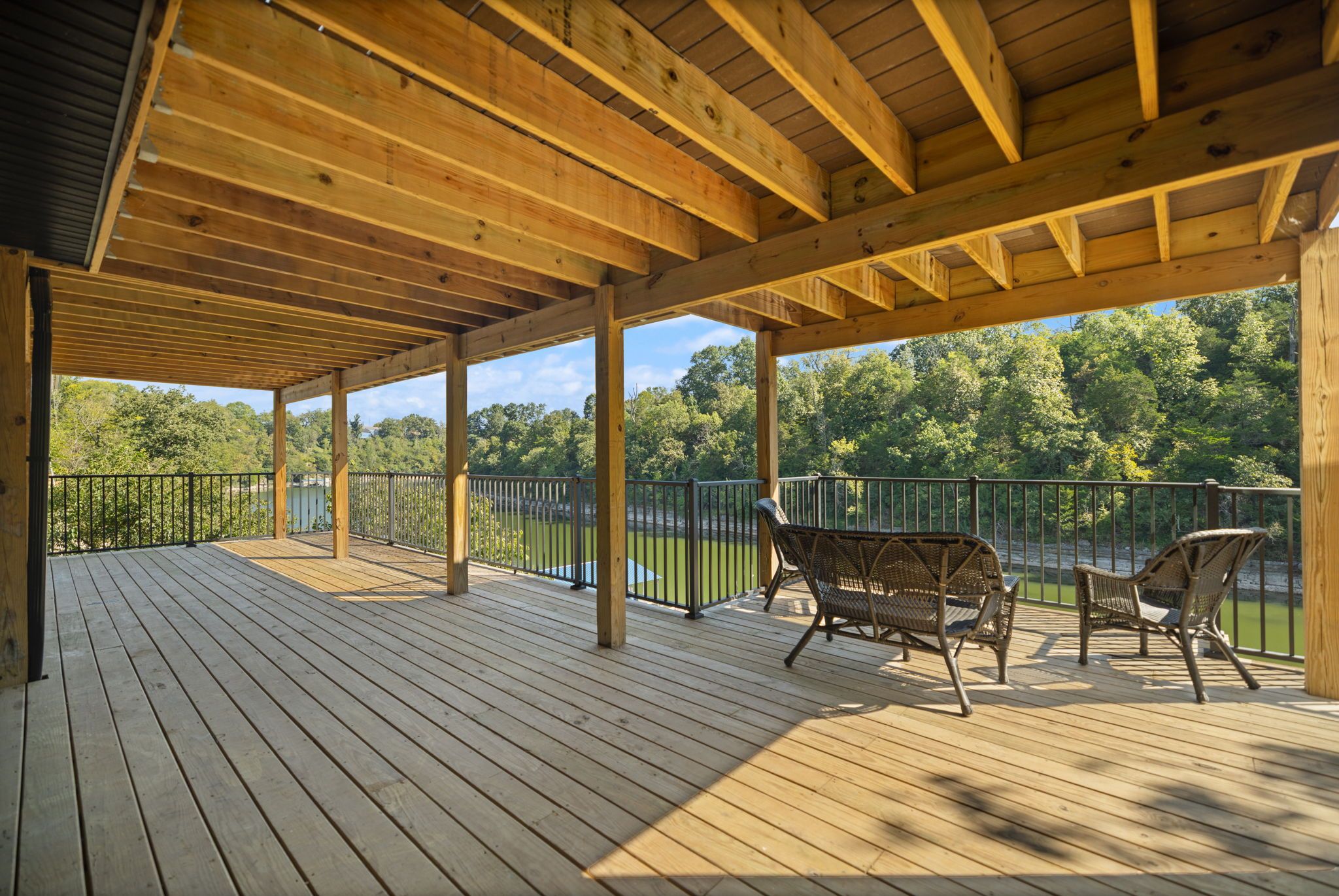 A wooden deck with a covered area, metal railings, and two wicker chairs.