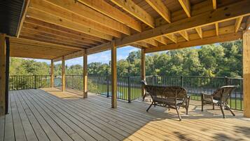 A wooden deck with a covered area, metal railings, and two wicker chairs.
