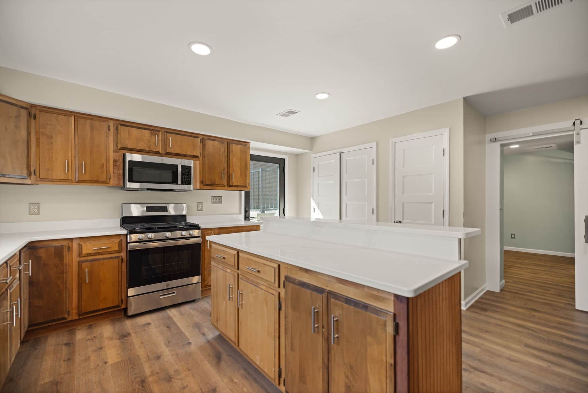 A modern kitchen with wooden cabinets, stainless steel appliances, and a white countertop.