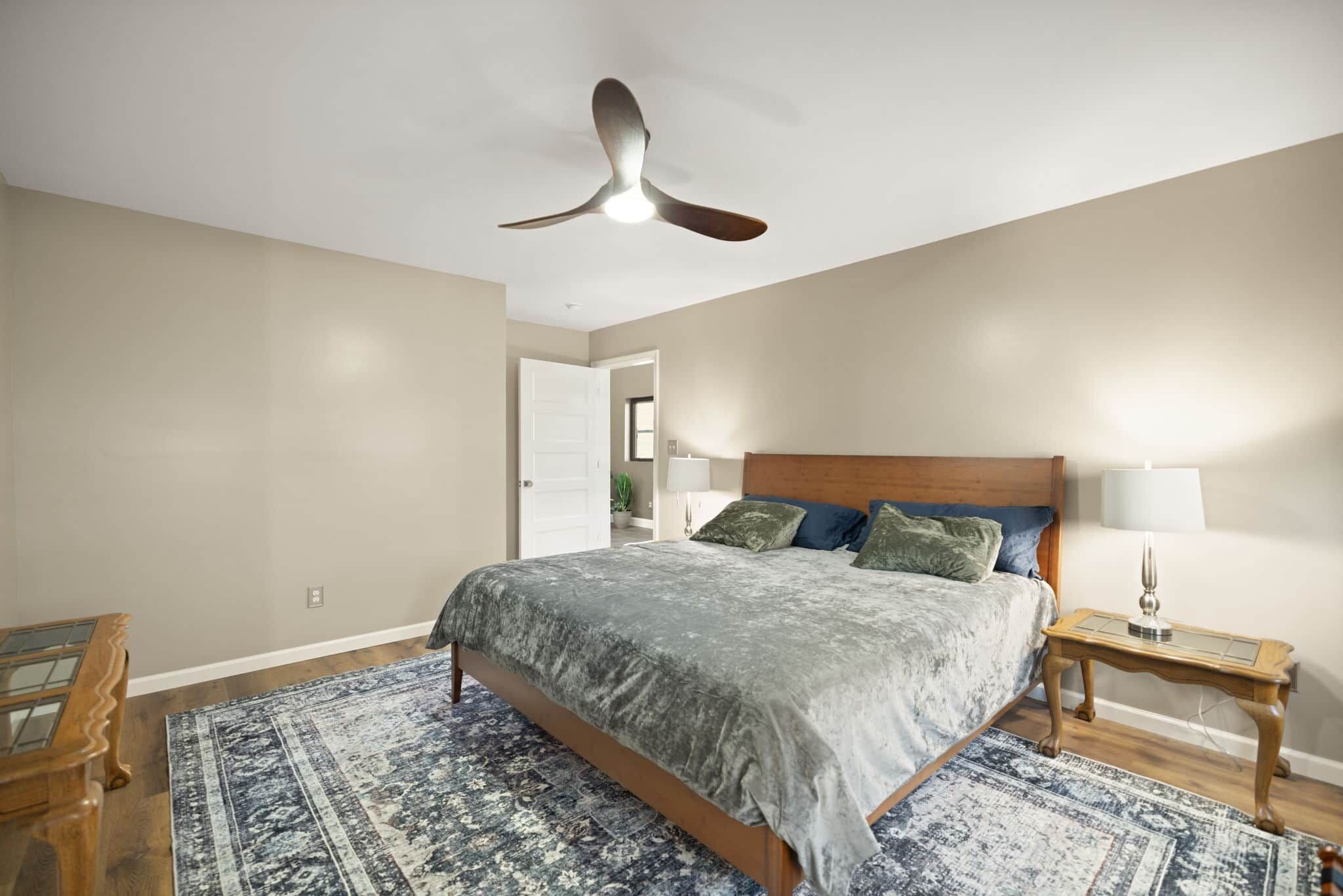 Una camera da letto con un letto, un comodino, una lampada, una ventola a soffitto e un tappeto decorato.