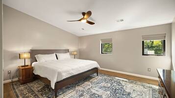 A bedroom with a bed, nightstands, a ceiling fan, and two windows.