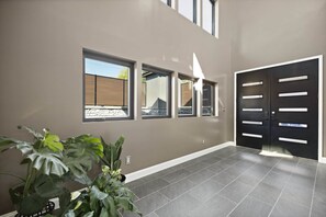 Un intérieur moderne avec un sol carrelé de couleur grise, une porte double noire et trois fenêtres équipées de stores.