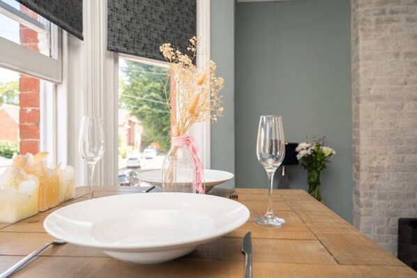 A dining table set with a white plate, a wine glass, and a vase with dried flowers.